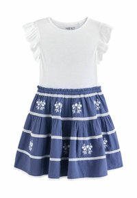 Vit kortärmad topp med volangdetaljer och en blå kjol med blommig broderi och horisontella vita ränder. Texturerad tyg.