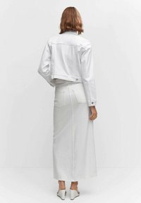 Giacca di jeans bianca con design accorciato e chiusure a bottoni, abbinata a una lunga gonna di jeans bianca con tasche posteriori e una trama senza cuciture.