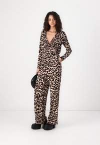 Mono de leopardo en tejido suave, con mangas largas, escote en pico profundo y piernas anchas. Combinado con zapatos de plataforma negros y una bolsa negra.