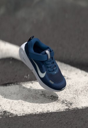 Modrá atletická topánka s textúrovaným sieťovinovým zvrškom, bielymi akcentmi, hladkou podrážkou a nastaviteľným remienkom; navrhnutá pre pohodlie a podporu.