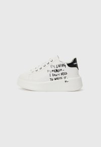 White platform sneakers with black accents, featuring a textured sole and handwritten text on the sides. Smooth leather material.