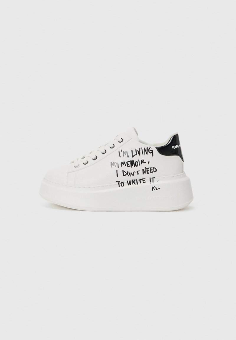 White platform sneakers with black accents, featuring a textured sole and handwritten text on the sides. Smooth leather material.