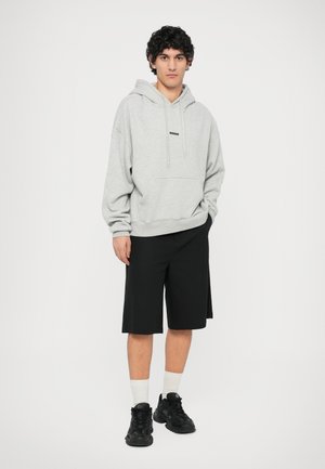 Gray hoodie with a kangaroo pocket and black branding, paired with black knee-length shorts and black sneakers with a textured pattern.