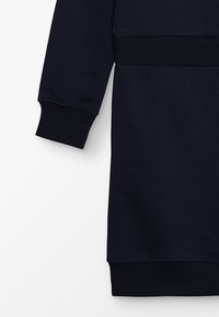 Granatowa sukienka sudadera z prążkowanymi mankietami i pasem. Charakteryzuje się miękką fakturą oraz prostym, nieskomplikowanym wzornictwem.