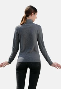 Pull en maille grise avec un col haut, présentant un motif en losange au dos et des manches longues ; associé à un jean noir ajusté.