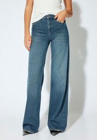 Jeans de mezclilla de pierna ancha en un lavado azul medio, con una cintura alta y un ligero desgaste, diseñados con bolsillos estándar y cierre de botón.