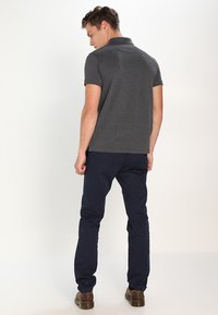 Polo gris à manches courtes, associé à un pantalon slim bleu marine et des chaussures marron, vu de dos. Texture lisse.