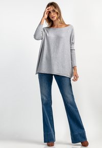 Jasnoszary, oversize sweter z szerokim dekoltem, w połączeniu z dzwonowymi niebieskimi dżinsami, które mają subtelną teksturę i widoczne szwy wzdłuż dołu.