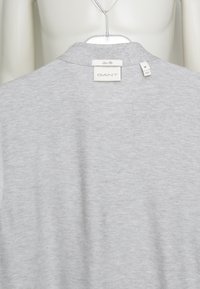 Chemise slim fit gris clair sur cintre montrant le col arrière avec l'étiquette de la marque GANT et l'étiquette de taille moyenne.