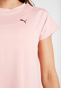 Camisa atlética de manga corta en color rosa, hecha de una tela suave, con un pequeño logo oscuro en la parte superior izquierda del pecho y un diseño simple y limpio.