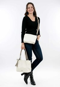 Sac à main en cuir blanc avec un accent de pompon et des poignées contrastées en beige, accompagné d'un plus petit sac bandoulière au design assorti.