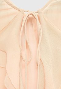 Peach fabric blouse featuring a soft, sheer texture with ruffled edges and a tie closure at the back, creating a delicate design.