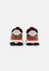 Nike sneakers with a black, tan, and cream mesh upper, red accents, and a white midsole featuring a textured black outsole.