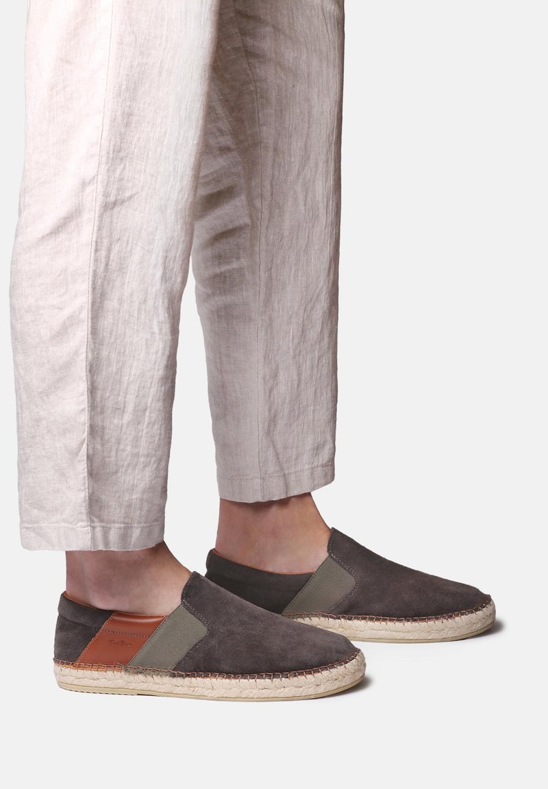 Jalad, mis kannavad tumedat halli libisevat espadrille-tüüpi kingi beeži nöörpõhjaga ja pruuni nahast kannaosaga, kombineeritud heledate beežide lühendatud pükstega.