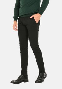 Pantaloni slim-fit neri realizzati in misto cotone, con una texture liscia e tasche laterali, abbinati a scarpe eleganti nere lucide.