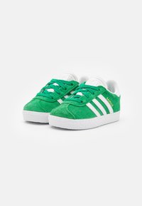 Green suede sneakers with white stripes, textured soles, and green laces. Brand name "Gazelle" in gold on the side.