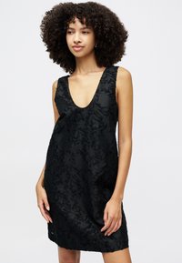 Juoda be rankovių suknelė su giliu iškirpimu, puošta tekstūriniais gėlėmis ir laisvu siluetu, pagaminta iš lengvos medžiagos.