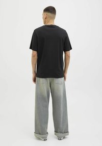 Camiseta de algodón negra de manga corta, corte relajado y cuello redondo, combinada con unos vaqueros de mezclilla de pierna ancha en gris claro con un acabado desgastado.