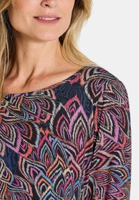 Multikleurige blouse met een bloemenpatroon in tinten roze, blauw en zwart. De stof heeft een zachte textuur en een ruime halslijn.