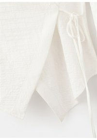 Tissu blanc matelassé avec un motif losange, bords pointus superposés et un détail de cordelette nouée sur le côté droit.