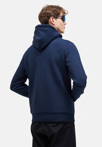 Felpa con cappuccio blu navy in morbido tessuto, dotata di tasca frontale e polsini a coste. Design elegante con una silhouette pulita.