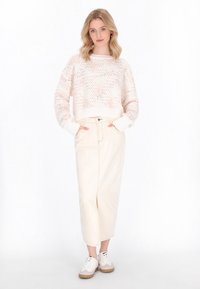 Strickpullover in hellem Creme mit zarten rosafarbenen Sprenkeln, kombiniert mit einem langen, cremefarbenen, hohen Rock mit einem Schlitz vorne und dezenten Metallakzenten.