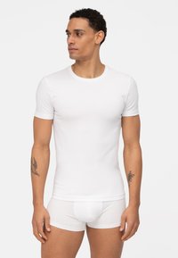 Weißes Baumwoll-T-Shirt mit kurzen Ärmeln, runder Ausschnitt, figurbetonte Form, getragen mit passenden weißen Boxershorts, glatte Textur.