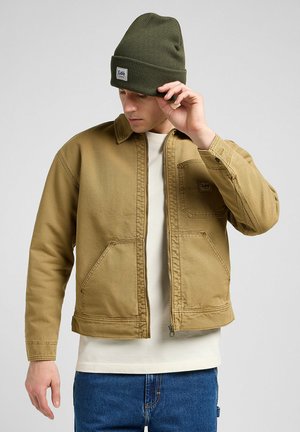 Braune Denimjacke mit Kragen und zwei vorderen Taschen, kombiniert mit einer grünen Strickmütze. Bietet einen Reißverschluss und sichtbare Nähte.