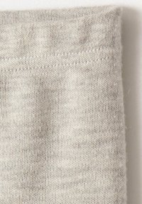 Tela gris claro con una textura suave y un ligero estiramiento. Presenta un dobladillo cosido en la parte superior y un patrón de punto consistente en toda su superficie.