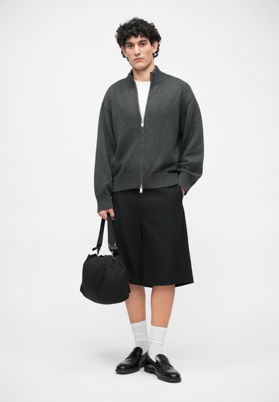 Mørkegrå zip-up sweater, sorte knælange shorts, sorte loafers, hvide sokker og en sort håndtaske. Enkel, ren design med minimale detaljer.