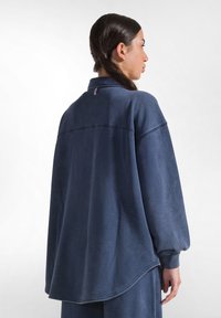 Felpa oversize blu scuro realizzata in tessuto morbido, con colletto alto, spalle scese e orlo curvo.