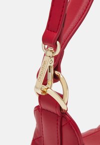 Bandoulière de sac à main en cuir rouge avec un clip en métal doré. Le matériau est texturé, avec des coutures visibles et un détail de marque.