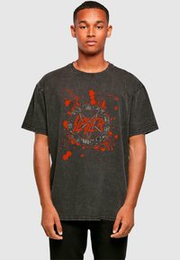 Svart oversized t-skjorte laget av bomull, med et rødt grafisk design med sprutmønstre og "Slayer"-tekst i en sirkulær utforming.