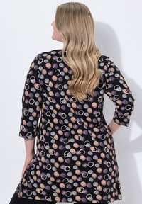 Schwarze Tunika mit einem Polka-Dot-Muster in Lila-, Pfirsich- und Grautönen, dreiviertel Ärmeln und einem abgerundeten Saum.