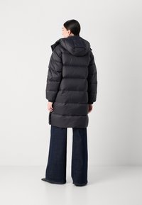 Svart dunjakke med hette, med horisontale quiltede seksjoner, elastiske mansjetter og design i mellomlengde, brukt med vide denimbukser.