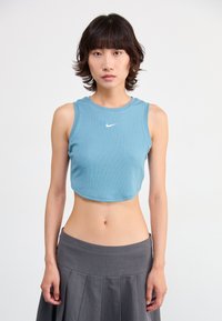 Light blue crop top, ribbed texture, sleeveless design, features small white Nike logo. Paired with a gray pleated skirt.