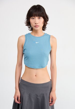 Light blue crop top, ribbed texture, sleeveless design, features small white Nike logo. Paired with a gray pleated skirt.
