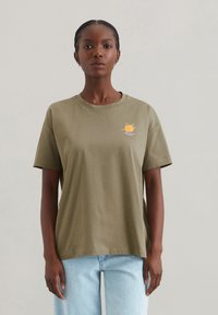 Olivgrünes Baumwoll-T-Shirt mit Rundhalsausschnitt, kurzen Ärmeln und einem kleinen orangen grafischen Design, das eine Biene zeigt. Lässiger Schnitt mit einer glatten Textur.