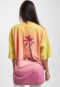 T-skjorte med korte ermer, oversized design, som har en gradient fra gul til rosa, med et palmetre grafikk på baksiden og en glatt bomullstekstur.