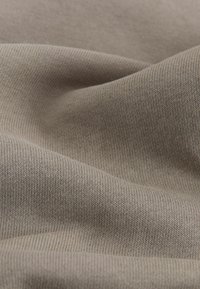 Strukturierter, hellbrauner Stoff mit einem feinen Strickmuster, das eine weiche und glatte Oberfläche mit subtilen Farbvariationen zeigt.