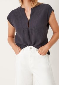 Haut court gris foncé à manches courtes avec un décolleté en trou de serrure et un tissu froncé. Associé à un jean large blanc, avec des poches latérales.