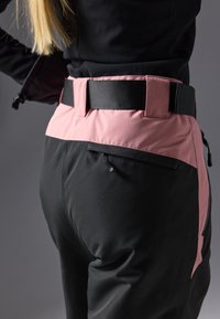 Black technical pants with a pink waistline feature a flat belt and zipper pocket. The fabric appears smooth and durable, designed for functionality.