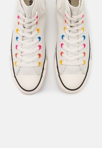Sneakers alte in tela bianca con occhielli multicolori e suole in gomma nera. Presentano lacci a contrasto in colori diversi.