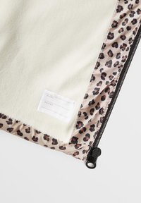 Torba wyłożona polarowym materiałem, z kremowym zewnętrzem i wnętrzem w panterkę, z zamkiem błyskawicznym oraz etykietą na imię i dane kontaktowe.