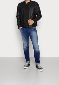 Svart läderbomberjacka över en svart t-shirt, kombinerad med ljusblå jeans och svarta lågt skurna sneakers med vita sulor.