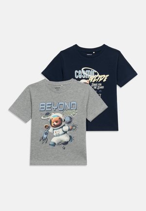 Δύο παιδικά μπλουζάκια, ένα γκρι με έναν αρκούδο αστροναύτη και το κείμενο «ΠΕΡΑ ΑΠΟ ΤΑ ΑΣΤΡΑ», ένα μπλε σκούρο με το κείμενο «ΚΟΣΜΙΚΗ ΣΤΑΣΗ» και γραφικά με θέμα το διάστημα.