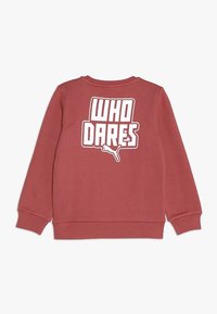 Sudadera de algodón roja con cuello redondo, mangas largas y un gráfico de texto blanco "WHO DARES" en la parte posterior en letras grandes.