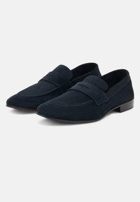 Mocassins pour hommes en daim bleu foncé avec des petits talons noirs et des brides décoratives sur le dessus, présentés côte à côte sur un fond blanc.
