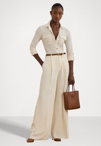 Kerman napitaitasu, joka sisältää kaksi rintataskua, korkeavyötäiset vaaleanbeiget leveälahkeiset housut, ruskea nahkavyö ja siihen sopiva käsilaukku.