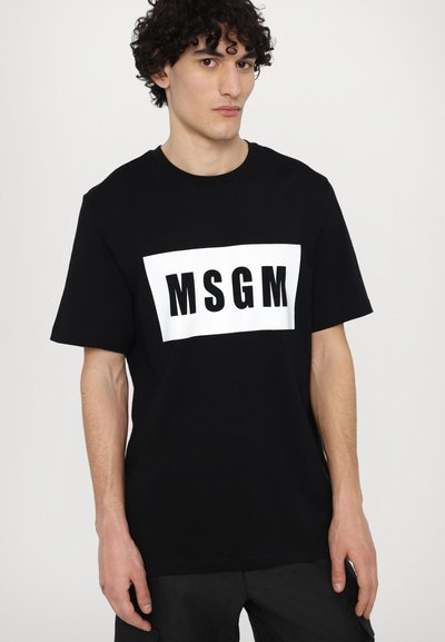 Svart bomull t-shirt med en rektangulär vit panel som har "MSGM" i fet svarta bokstäver. Korta ärmar, avslappnad passform och rundad halsringning.